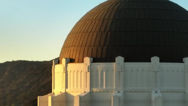 映画の黄金の時間の日没の光でグリフィス天文台ドームの背後の動きの背景に現れるハリウッドのサインの息をのむような航空機 ハリウッド レターズ ドローン Los Angeles Usa — ストック動画