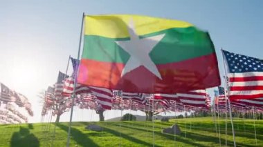Myanmar ya da Burma bayrağı rüzgarda dalgalanırken arka planda birçok Amerikan bayraklarıyla altın günbatımında güneş parlamasıyla birlikte. Ulusal Myanmar veya Burman bayrağı bağımsızlığı görselleştiren ekonomi ortaklığı