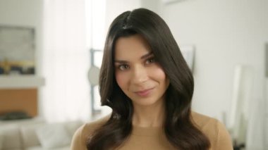 Parlak modern arka planda kameraya bakarak flört eden genç, lüks, seksi esmer kadının yakın plan portresi. Kahverengi gözlü ve doğal makyajlı zarif modelin yüzü yavaş çekimde.
