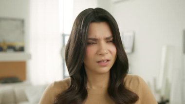 Acı verici baş ağrısı konsepti. Ağır çekimde anksiyete ağrısı, zihinsel stres, panik atak, ağrıyan baş. Hüsrana uğramış, sinirli esmer kadın modern evde baş ağrısı ile baş ediyor.