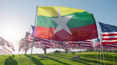 Myanmar ya da Burma bayrağı rüzgarda dalgalanırken arka planda birçok Amerikan bayraklarıyla altın günbatımında güneş parlamasıyla birlikte. Ulusal Myanmar veya Burman bayrağı bağımsızlığı görselleştiren ekonomi ortaklığı