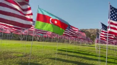 Azerbaycan bayrağı rüzgarda dalgalanırken Amerikan bayrakları hareket halindeyken altın günbatımında güneş parlamasıyla birlikte. Ulusal Azerbaycan bayrağı bağımsızlığı, mali ekonomiyi ve iş ortaklığını görselleştirdi