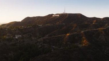 İkonik Amerikan simgesi, Kaliforniya 'nın batı kıyısına seyahat. Hollywood tabelası parlak gece aydınlatması 4K. Los Angeles 'ın altın günbatımında büyük beyaz harflerin havadan görünüşü. Los Angeles ABD Şubat 2023