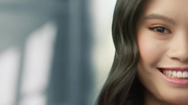 Gri, tarafsız arka planda kapalı alanda poz veren güzel Çinli kızın güzel yüzü. Etnik konsept yakın plan portre, gerçek insanlar 4K çekimi. Gözleri harika Asyalı gülümseyen kadın dik dik bakıyor