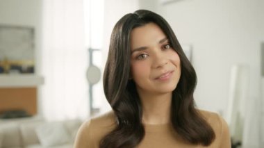 Güzel bir kıza tatlı bir şey dokunur. Gündelik bej süveter giyen güzel, esmer bir kadın parlak, modern bir evde poz veriyor. İnsanların yaşam tarzı konsepti. 4K sevimli yüzlü kamera.