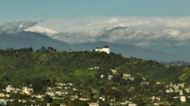 Sinematik California tarihi Griffith gözlemevi ve hareket arka planında manzaralı bulutlarla kaplı yeşil tepelere park. Los Angeles ABD 'nin manzaralı helikopter görüntüsü