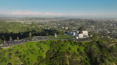 Griffith Gözlemevi 'nin ve Hollywood Dağı' ndaki yeşil parkın güneşli yaz gününde mavi gökyüzünün altında harika bir manzarası var. Girişteki çimen gözlem güvertesi, Los Angeles şehir manzarası hareket arka planı, Kaliforniya