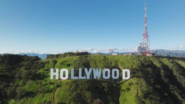 青い空の下の緑の丘の上のハリウッドの標識のゆっくりとした動き 巨大な白い文字 カリフォルニア州の米国のシンボルにヘリコプターの接近ビュー 休暇観光の概念 ロサンゼルス California Usa 2023年3月 — ストック動画