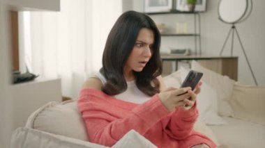 Kanepede oturan endişeli kadın elinde akıllı telefonuyla e-banka uygulaması kullanarak güvensiz online ödeme yapmaya çalışıyor. Para yüzünden sorunlarla yüzleşen bir kız. Banka dolandırıcılığı sorunu, başarısız işlem kavramı