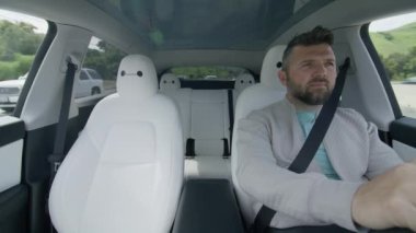 Güneşli yaz gününde otomatik pilot teknolojisini kullanan, Tesla Model Y 'nin içindeki olgun erkek sürücü. Çevre dostu, modern elektrikli araba kullanan yakışıklı bir adam. Tren yapay zeka sürücüsü sistem araçlarını izliyor