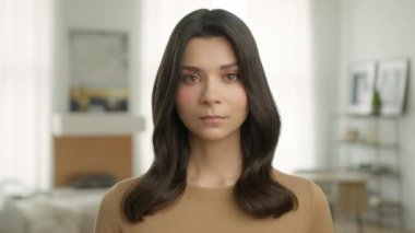 Bej rengi günlük hırkalı, sağlıklı, parlak saç stili olan güzel, melez bir kadının portresi evde kameraya bakıyor. Üzgün, Latin, esmer kızı kapatın.