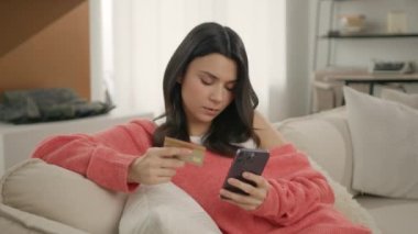 Kredi kartlı sakin bir bayan internet üzerinden ödeme yapmak için akıllı telefon kullanıyor, tüketici ürünleri alıyor, evden ekommerce sitelerinden sipariş veriyor. Odaklanmış genç esmer kadın Ebank 'in güvenli işlemini yapıyor.