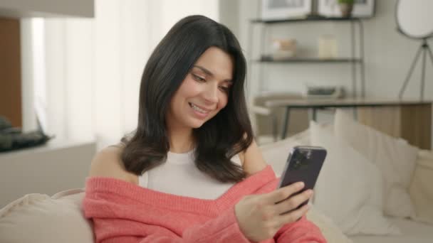 Munter Ung Smuk Kvinde Bruger Smartphone Mens Sidder Sofaen Smilende – Stock-video