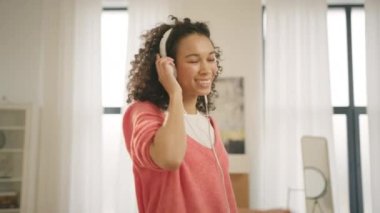 Genç Afro-Amerikan 'ın sinematik görüntüleri beyaz kulaklıklarla müzik dinlerken çılgınca dans ediyor. Kapalı gözlü siyahi kadın popüler müzikten hoşlanıyor, modern daire 4K 'de tek başına eğleniyor.