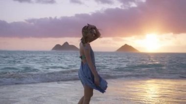 Güzel, el sallayan bir elbise giymiş bir kadın sinemada pembe gün doğumunda. Ağır çekim kadın manzaralı plaj manzarasının keyfini çıkarıyor. REC kamera 4K. Oahu Hawaii Adası ABD 'de yaz tatilindeki kadın turist.. 