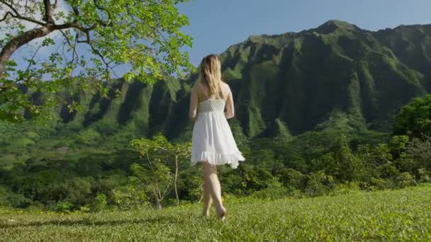戻る若い女性が離れて歩いて 腕を上げて 映画のような緑のジャングルの山々の背景で回って表示します 幸せな本物の女の子ターン周りに熱帯のエキゾチックなハワイの自然景観 — ストック動画