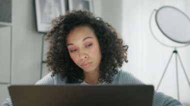 Laptop bilgisayarında çalışan düşünceli afro bir kadın ev ofisindeki sorunu çözmeyi düşünüyor. İlham arayan ciddi bir kadını kapatmak, fikir eksikliği hissetmesini sağlamak.