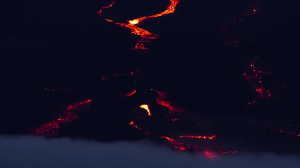 ハワイアメリカのビッグアイランドの下方で渦巻く雲の上の距離で見られる 輝く溶岩の流れの壮大なショット マウナロア山の国立公園活動的なキラウエア火山 夜には熱い溶岩流が流れる — ストック動画