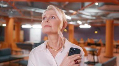 Modern ofiste akıllı telefon üzerinde çalışan düşünceli bir iş kadını. İş geçmişine bakan kadın yöneticinin portresi. Kapalı alanda iş yapmayı düşünen ciddi şüpheli bir iş kadını.
