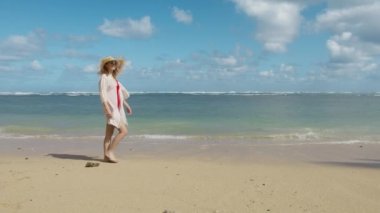 Romantik bir kadın deniz mavisi suyla beyaz kumlu sahilde yürüyor. Hawaii sahilinde güzel bir okyanus arka planında dinlenen kadın. Moda modasına uygun bir kız. Seyahat tatili, yaz tatili.