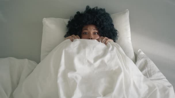 恐怖に満ちたアフリカ系アメリカ人女性がベッドで毛布から顔をのぞかせ カメラを向ける 白い枕の上に快適なベッドの中で色のトップビューのクローズアップ女性 — ストック動画