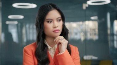 Ofiste duran düşünceli, genç Asyalı stil sahibi iş kadını dikkatle dinliyor. Kapalı alanda yakın plan portre için poz veren güzel yüzlü konsantre profesyonel bir kız.