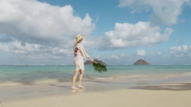 Güzel bir Amerikalı kadın yaz tatilinde eğleniyor. Mutlu gülümseyen neşeli kız dans eden Oahu. Havai adasında kırmızı mayo, plaj örtüsü ve hasır şapka giyen heyecanlı ve neşeli bir bayan.