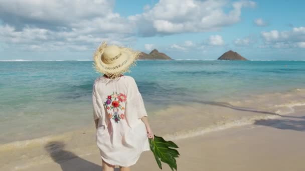 ハワイの有名な目的地を訪れる旅行者のインフルエンサー パラダイスLanikaiビーチでの休暇の女性 オアフ島の休日 リゾートホテル4Kで豪華な旅行で巨大な緑の葉を持つわらの帽子の女の子 — ストック動画