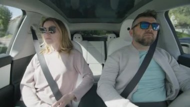 30 'lu yaşlarda kadın ve 40' lı yaşlarda erkek, çevre dostu modern elektrikli arabada konuşuyor. AI sürücüsü sistem araçlarını izliyor. Otomatik pilot teknolojisini kullanarak güneşli bir yaz gününde arabadaki adam sürücü.
