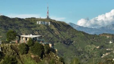 Hollywood Hills 'teki pahalı evlerin sinematik çekimleri. Arka planda ünlü Hollywood tabelası ve parallax efektli. Hava helikopteri yeşil tepeler güneşli bir günde Los Angeles, ABD, Mart 2023