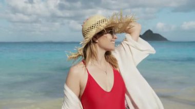 Açık deniz seviyesinde genç bir kadının portresi. Hawaii plajındaki güzel moda kadını Hawaii adasındaki büyük hasır şapkalı güneşin tadını çıkarıyor. Doğaya bakan büyüleyici kızın yüzünü kapat.