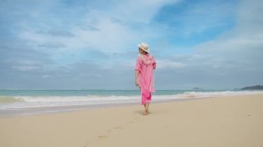 Güneşli yaz gününde beyaz kumlu sahilde yürüyen güzel pembe gömlekli genç bir kadının yavaş çekim arkası görüntüsü. Hawaii Oahu 'da yaz tatilindeki kadın turist.
