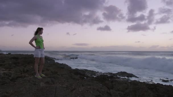 日落时分 旅行妇女享受着美丽的大海广阔的风景 天空是紫色的云彩 美丽的蓝色大海和平静的巨浪漂浮在太平洋的岩石海岸上 夏威夷景观背景 — 图库视频影像