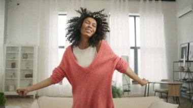 Yavaş çekim güzel siyah kadın afro saçlı, gülümseyen ve dans eden şık modern tasarım çatı katında parlak pencereli arka planda. Mutluluk ve eğlence zamanı konsepti video 4K