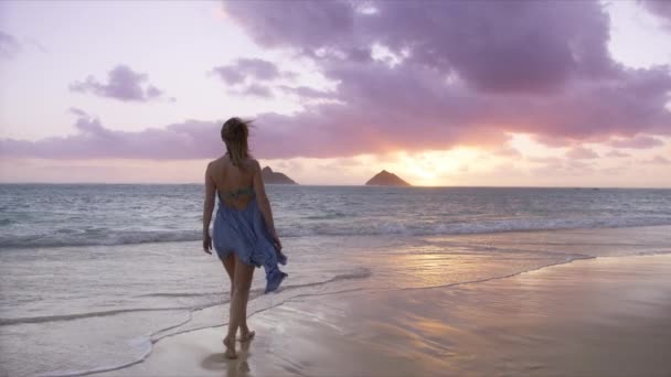 黄金の日の出のビーチで裸足で歩くスローモーションの女性 オアフ島の夏休みの女性観光客ハワイ島アメリカ 女性で美しい手振りドレスで映画黄金の日の出 Recカメラショット — ストック動画