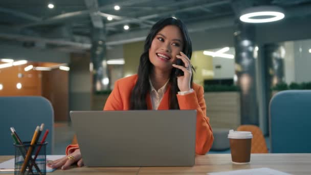 兴奋的年轻亚裔美国女商人在办公室里享受着成功的工作计划 有道德的女人坐在办公桌前 开着笔记本电脑 用智能手机交谈 开心地庆祝好消息慢下来 — 图库视频影像