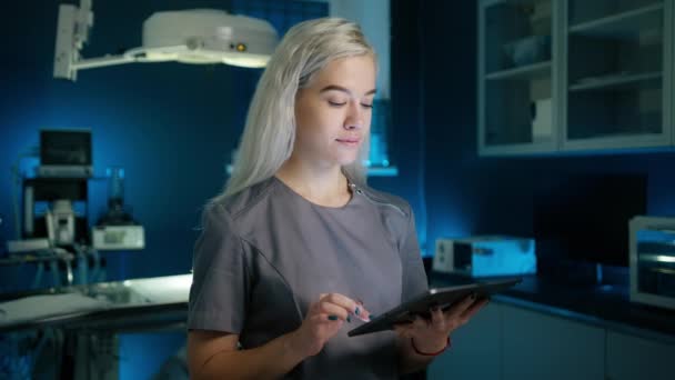 ブロンドの女性獣医師の肖像画 動きの背景に現代の獣医学クリニックでペットのタブレットコンピュータ上でX線スキャンをレビューします チェックアップ手順 試験防止コピーの背景 — ストック動画