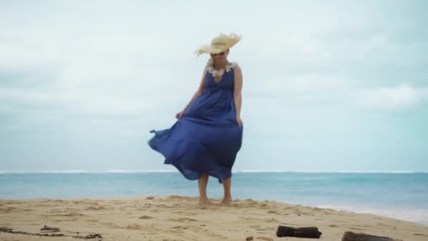 在夏威夷的瓦胡岛上 身穿海滩马西裙 头戴大草帽的年轻女子在沙滩上跳舞 在蓝色的大海中打转 欣赏大海的美景 在美国的红色4K旅游中拍摄 — 图库视频影像