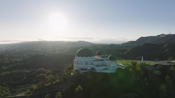 グリフィス天文台ドームと緑の芝生の展望台の上の叙事詩のマラリア 光沢のあるレンズフレアと晴れた夏の日没のハリウッド山の緑の公園 ロサンゼルスの街並み California Usa 2023年3月 — ストック動画