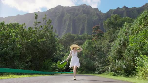 緑の自然を歩き 手に巨大な熱帯植物の葉を放棄若い幸せなスリムなヒップスター女性 ボホスタイルの夏服 夏のわら帽子の候補の女の子で高い緑の山の背景ハワイ — ストック動画