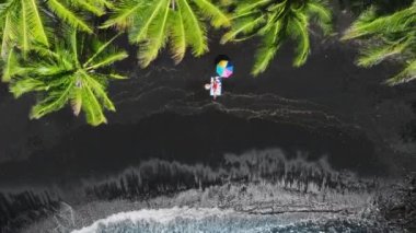 Plajda havluyla güneşlenen tatilci kadın Hawaii adasındaki karanlık volkanik plajda güneşleniyor. Renkli güneş şemsiyesinde güneşlenen turist kız seyahatin tadını çıkarıyor. Lüks yaşam tarzı.