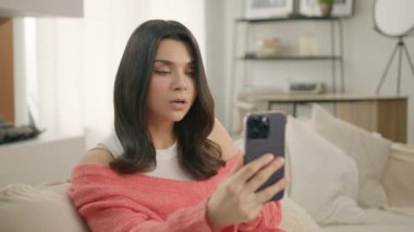 Evdeki oturma odasında akıllı telefon kullanarak konuşan esmer bir kadın şaşırdı. Heyecanlı, aktif ve şık giyinmiş bir kız. Cep telefonu kullanıyor. Teknoloji yaşam tarzı kullanımı kavramı