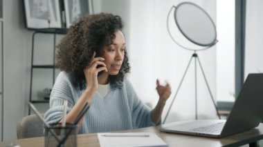 Akıllı telefonu olan aktif bir iş kadını dizüstü bilgisayar ekranına bakarak konferans görüşmesi yapıyor. Karışık ırk profesyonel halkla ilişkiler müdürü uzaktan mobil konuşma, iş görüşmesi ev bilgisayarı ofisi.