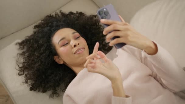 在家里的年轻非洲裔美国妇女通过视频电话或使用手机的社交网络与朋友或情人男友交流时 形象上的正面满足令她们满意 梦幻般的非洲裔美国女孩沙发 — 图库视频影像