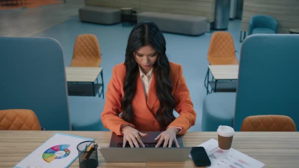 フォーカスされたアジアの女性20代のマネージャービジネス女性は 現代のロフトオフィスでラップトップコンピュータに入力作業机の上に座って 疲れて後ろの頭の後ろに手を置く4 Kをストレッチするために椅子にもたれて — ストック動画