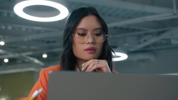 穿着眼镜的聪明的亚洲女人的近照 女老板在模糊的背景下 在现代开放式阁楼办公室工作 创业者在笔记本电脑上输入电子邮件 阅读新闻4K — 图库视频影像