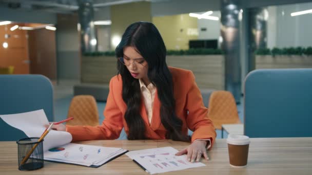 レポートテーブルを見て疲れたストレスの少女は 空のオフィスで深夜に懸命に働いている間 彼女の頭を手でつかむ 書類を机の上で書類審査するアジアのビジネス女性の疲れ — ストック動画