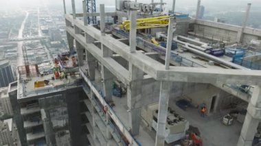 Mimarlar ve inşaatçılardan oluşan çeşitli ekiple birlikte emlak projesinde çalışan yeni inşaat alanının üzerinde havadan uçuş. Gökdelen çatısında ağır makineler ve inşaat işçileri