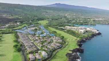 Pasifik Okyanusu manzaralı, volkanik Hawaii Adası 'ndaki yeşil golf sahasıyla çevrili sahil kulübelerinde hava manzaralı drone manzarası. Hawaii 'deki tropikal ormanlardaki lüks deniz kıyısındaki tatil beldesinde yaz tatili