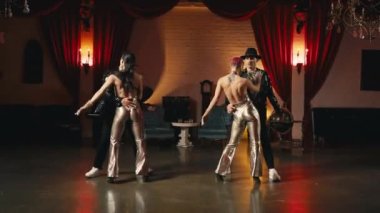 Grup dansçıları senkronize koreografiyi hareket ettiriyor. Altın renkli şık kıyafetler içinde modern dansçılar ağır çekimde. Altın Hollywood tarzı gece kulübündeki etkileyici gösteri performansı.